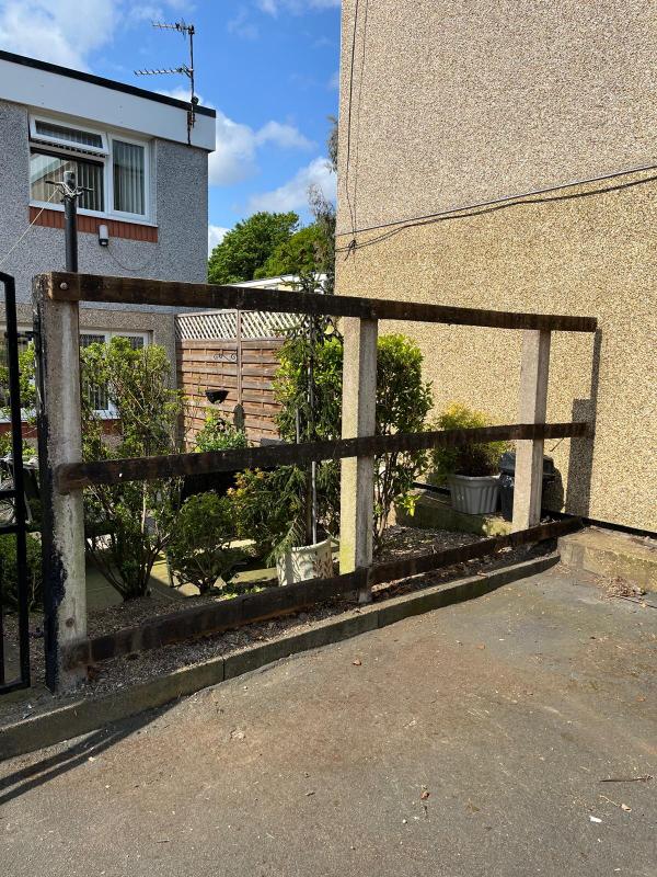 Old rotten timber railings on concrete posts along a driveway boundary